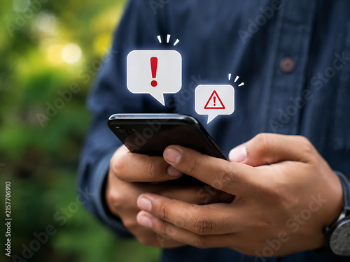 Man holding smartphone with notification bubbles displaying warning and alert symbols outdoors