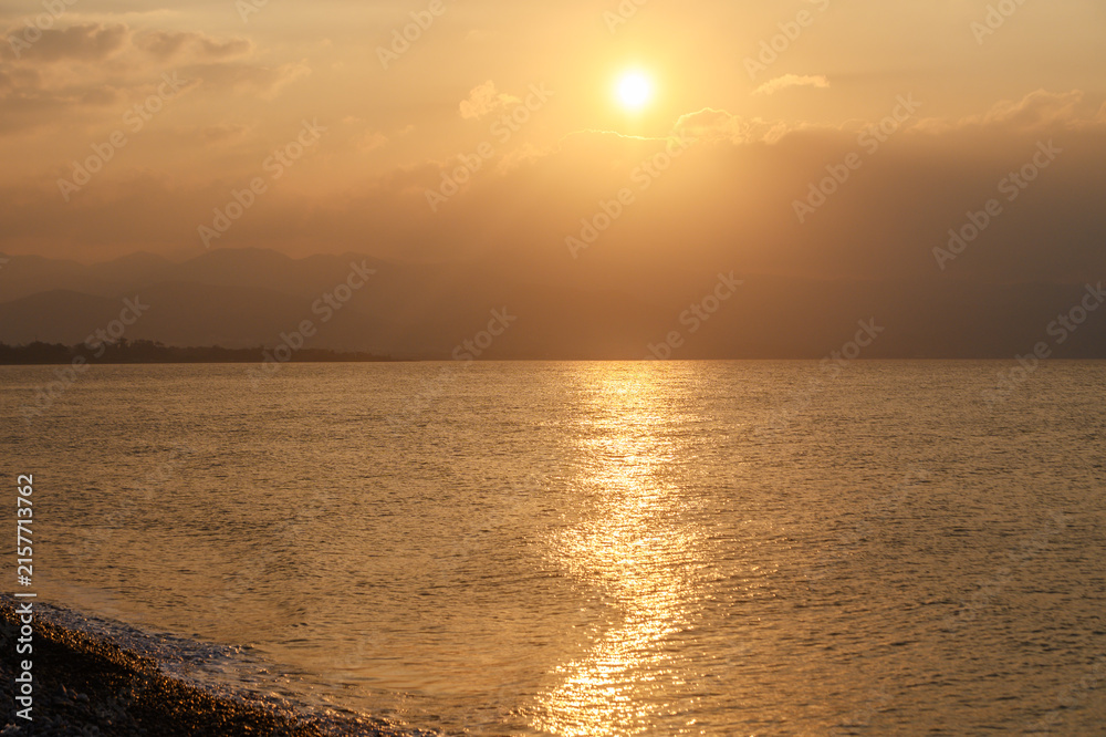 Obraz premium Golden sunset illuminates serene waters and distant mountains in a tranquil coastal escape