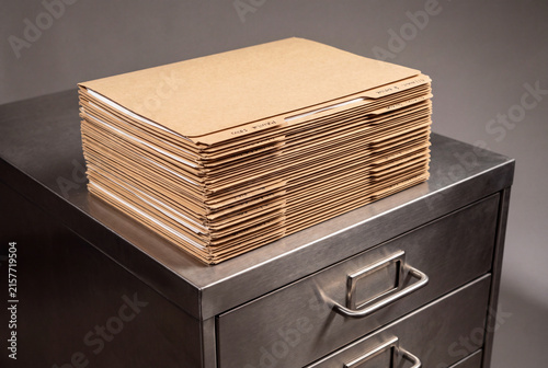 Stack of brown manila file folders resting on a brushed metal cabinet