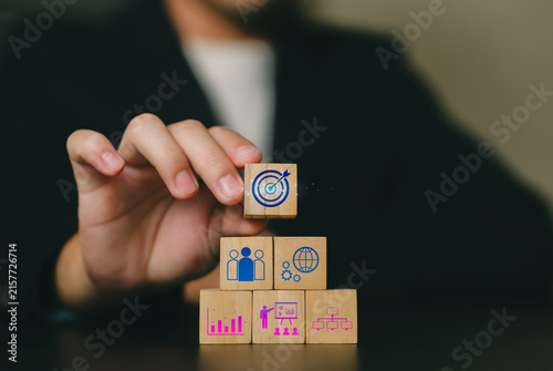 A professional holding a small wooden block with a target symbol above other stacked blocks representing analysis, planning, growth, and strategic success.