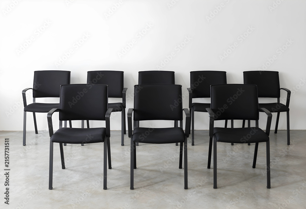 Obraz premium Empty black office chairs arranged in rows against a white wall, ready for a meeting or conference, business and corporate setting