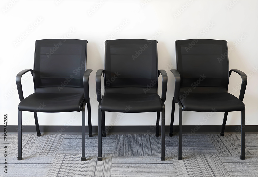 Obraz premium Three empty black office chairs in a row against a white wall, waiting room or reception area seating