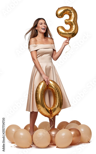 Young woman celebrating thirtieth birthday holding large gold balloons with birthday celebration balloons anniversary