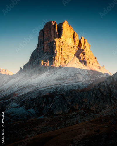 Dolomites mountain peak glowing in golden morning sunlight with clear blue sky in Italy