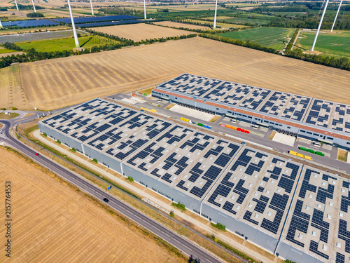 Bild auf Leinwand Solar panels on warehouse rooftops in a rural area with wind turbines nearby and