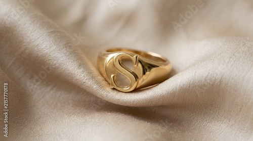 Close-up of elegant gold initial ring resting on soft pink fabric for luxury branding