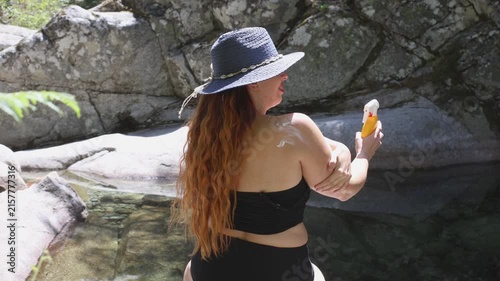 Rear view of a red-haired woman applying sunscreen next to a natural river pool, Gredos, Spain.