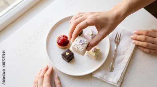 Hands picking up a gourmet petit four from a plate of assorted luxury French pastries