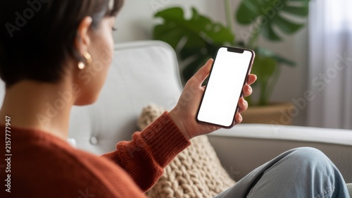 Woman holding smartphone with blank white screen mockup at home