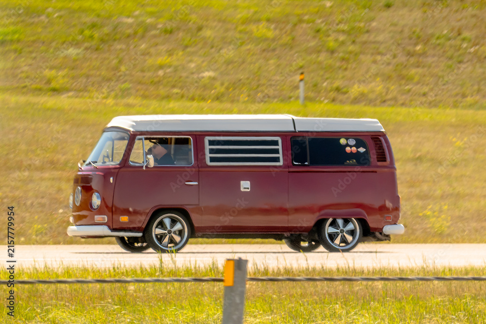 Fototapeta premium Calgary, Alberta, Canada. August 15, 2026. Side view of vintage red Volkswagen Westfalia camper van driving along highway on sunny day.