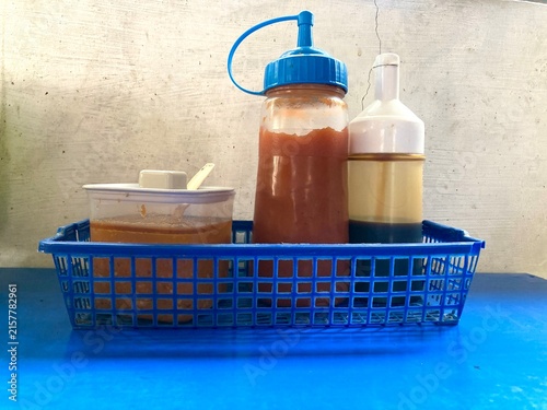 Indonesian street food condiments including chili sauce, soy sauce squeeze bottles, and a container