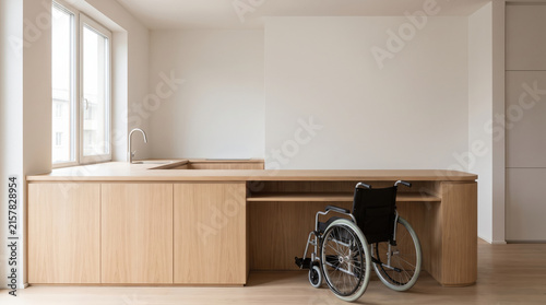 Accessible kitchen counter with wooden cabinets and wheelchair in bright room with natural light