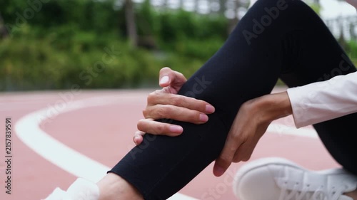 Close-up of Asian woman holding her painful calf on running track during workout. Calf muscle strain, leg cramp, runner injury, sports accident, and healthcare concept.