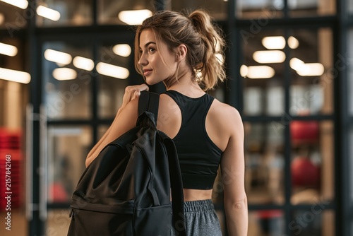 Young athletic woman with ponytail carrying a black backpack at the gym  ready for workout