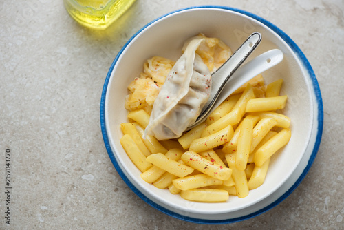 Korean tteokbokki or garaetteok served with steamed dumpling and egg in a white and blue bowl, horizontal shot on a beige stone background, high angle view