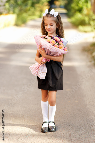 Fotografía Charming little schoolgirl holding flower bouquet on her way to school on autumn