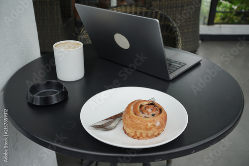 Quadro su tela Home bakery Danish pastry cake on dish and laptop on the table.