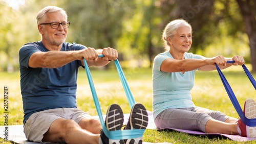 Active senior couple exercising with resistance elastic bands on yoga mats in park