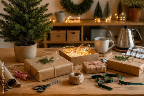 Gift wrapping corner with potted fir, string lights, wrapped boxes, and steaming mug