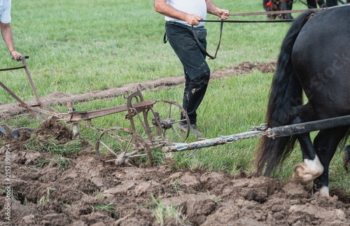 Ploughman Guiding Antique Wheeled Plow Through Wet Soil