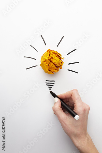 human hand drawing a light bulb on paper. flat lay abstract composition with innovation elements. Human finger touches a bright yellow crumpled paper ball shaped like a light bulb drawn on a textured.