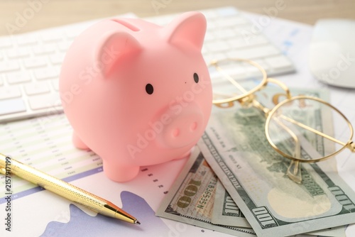 Fotografía Piggy bank, dollar banknotes, documents, glasses, pen and keyboard on table, clo