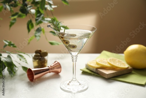 Foto Martini cocktail with olives in glass, lemons, jigger and green plant on white t