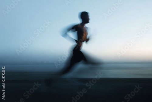 Blurred motion silhouette of a runner on the shore for dynamic background and fitness banner design with soft blue dusk tones