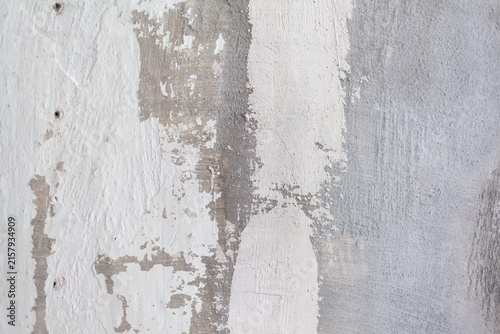 Textured wall features peeling paint in white and gray tones, exposing layers of plaster and concrete, creating a weathered appearance