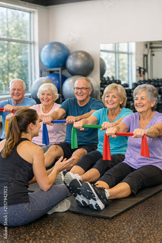 A group of seniors participating in a gym fitness class, exercising with resistance bands and focusing on their overall well-being