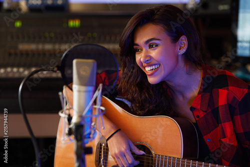Woman singer in studio. Young artist with guitar recording her song.