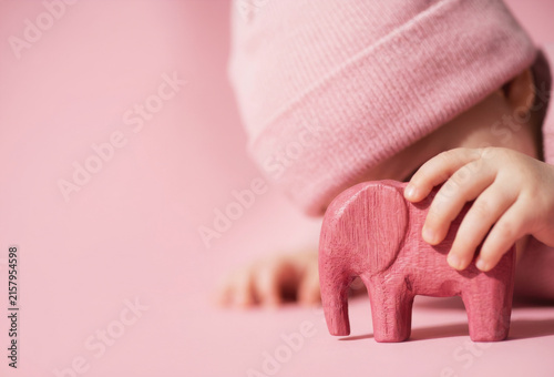 Toddler wearing a pink beanie playing with a wooden elephant toy