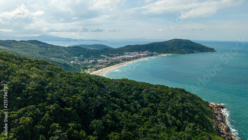 Aerial view of Praia Brava beach surrounded by lush Atlantic forest, turquoise ocean waters, and coastal buildings in Florianopolis, Santa Catarina, Brazil.
