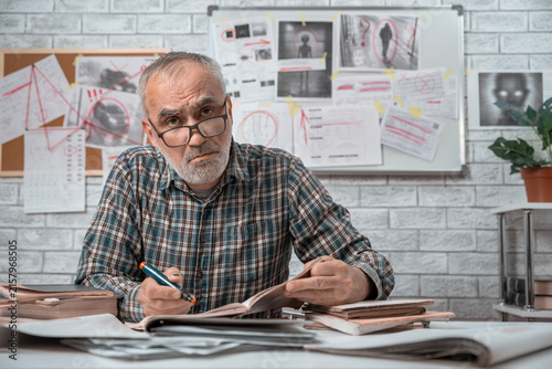 Foto and taking notes in front of a board covered with clues, and mysterious images in the background