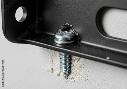 Close up of silver screw mounting black metal bracket on drywall.