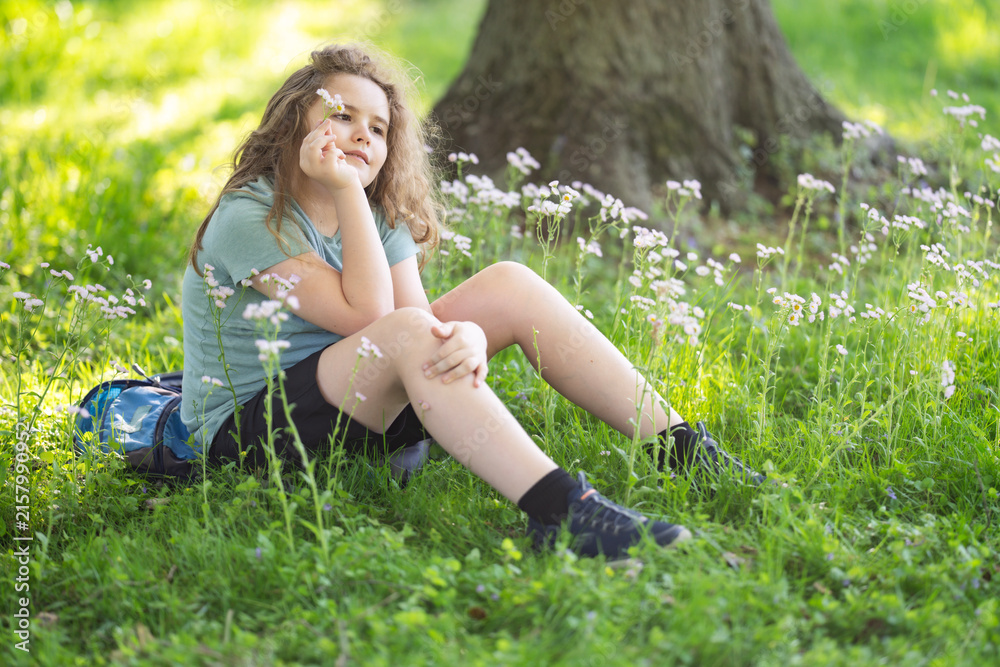 Naklejka premium Child portrait shows summer innocence. Relaxed child sits in green meadow. Smiling child enjoys sunny nature. Child lifestyle feels peaceful and authentic.