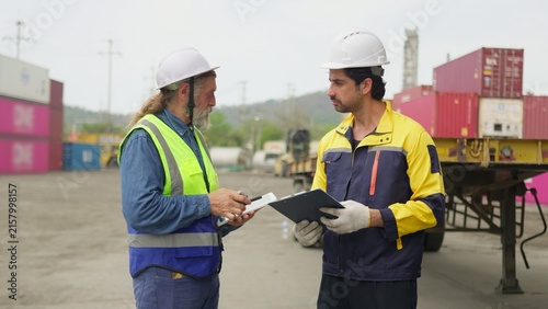 Fotografía Two logistics workers discuss a shipping manifest on a clipboard in a container yard, collaborating on supply chain management and cargo inspection, reflecting teamwork and modern workplace themes