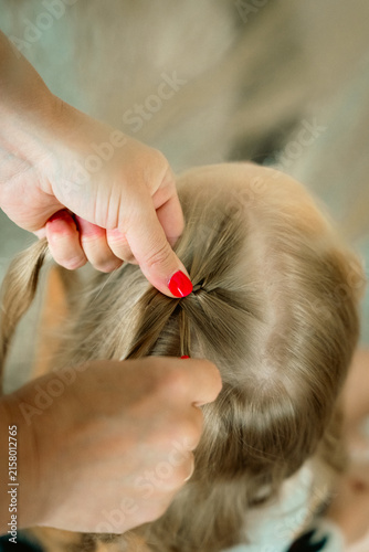 фотографія Adult hands braiding a child’s long blonde hair in a close-up view from behind