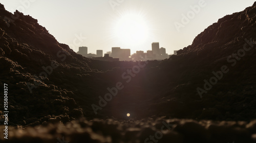 City skyline silhouette seen in backlight through a gap in rough black rocks in the foreground.