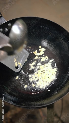Cooking Thai stir-fried flat rice noodles with pork and dark soy sauce (Pad See Ew Moo). Searing wide rice noodles in a hot cast iron wok, sauteing garlic, fresh Chinese kale, and tender sliced pork