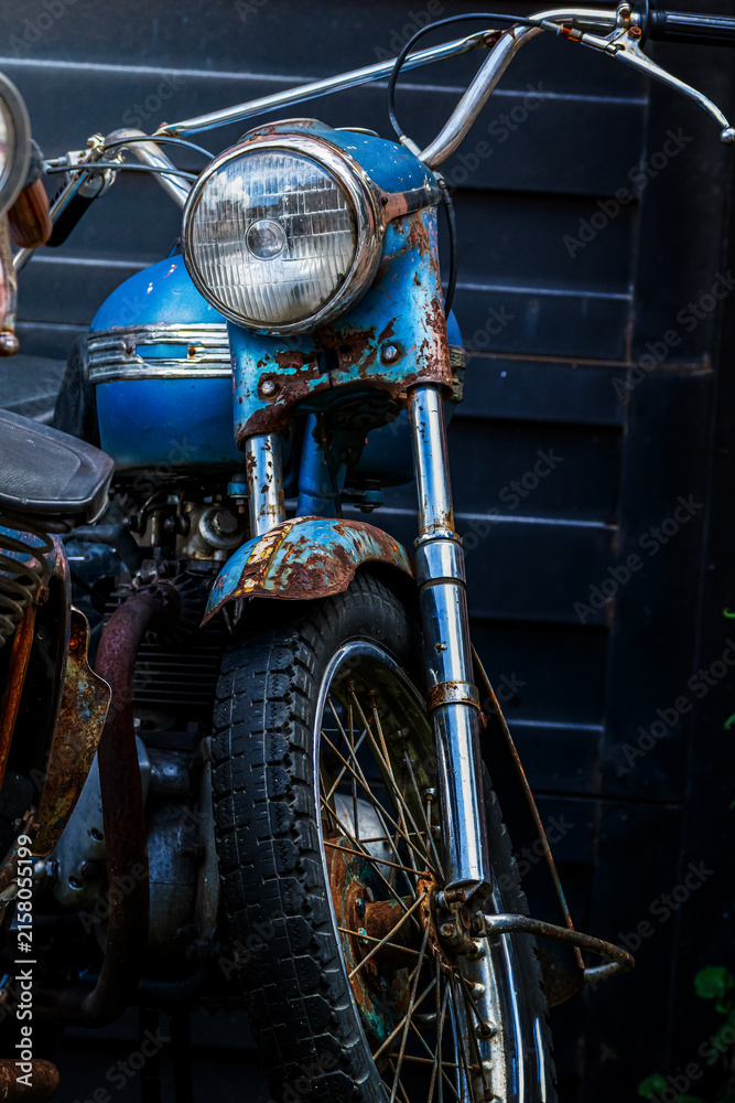 Fototapeta premium Vintage Rusted Blue Motorcycle Front View Close-Up with Classic Round Headlight and Chrome Handlebars in Dark Garage Setting