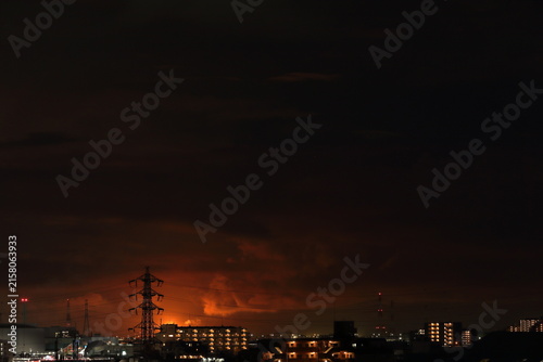 光害：フレアスタックの炎が照らす雲と都市の夜景 / Light pollution: Flare stack flames illuminating clouds over a city at night