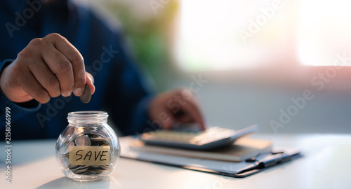 Close-up of man hand putting coins in glass bottle saving bank for account save money. Planning step up, saving money for future plan, retirement fund. Business investment-finance accounting concept.