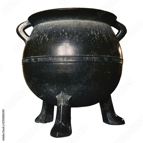 A big black cast iron metal cauldron in a medieval castle basement under an arch