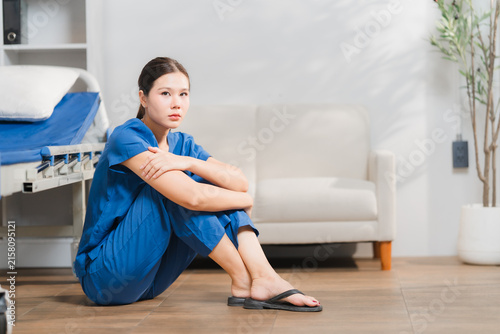 Quadro su tela Weary Caregiver's Solitude: A nurse in blue scrubs sits dejectedly on the floor beside a hospital bed, her face etched with fatigue and despair, reflecting the emotional toll of her profession