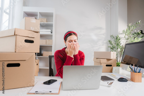 Canvastavla Frustrated Entrepreneur: A young woman sits at her desk in a home office cluttered with shipping boxes, covering her mouth and nose as if to suppress a sneeze or stifle a cough