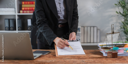 Obraz na plátne Legal Consultation: A meticulous legal professional reviews a document on a clipboard, surrounded by law books, a scale of justice, and office essentials, representing diligence and legal expertise