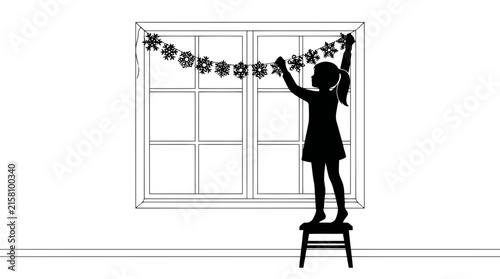 Silhouette of a young girl standing on a small stool reaching up to hang a festive snowflake garland on a large window