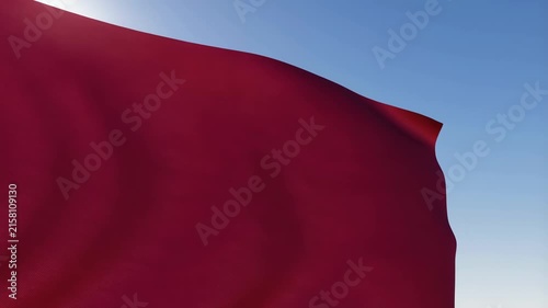 Red Flag Waving in Bright Sunlight Against Clear Blue Sky