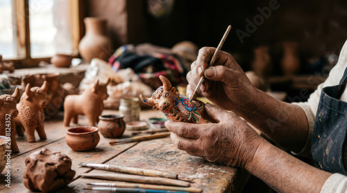 Artist hands painting small ceramic animal figurines on a wooden table.